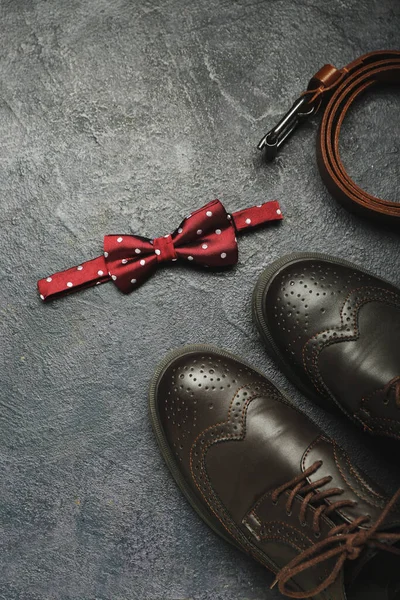Stylish male bow tie, shoes and belt on dark background