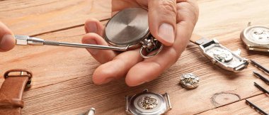 Erkek saatçi masadaki bozuk saatleri tamir ediyor.