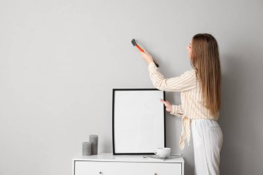 Young woman hanging blank frame on grey wall at home