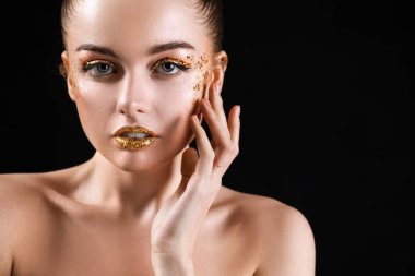 Young woman with golden glitter makeup on black background, closeup