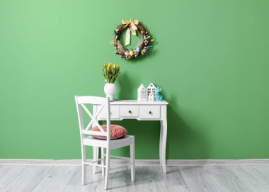 Table with tulips, candle holders, rabbit and Easter wreath on green wall