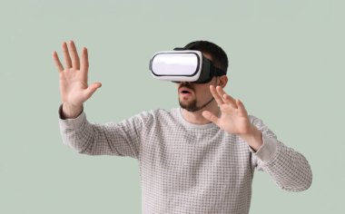 Yeşil arka planda VR gözlüğü kullanan genç adam.