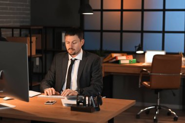 Erkek muhasebeci geceleri ofiste bilgisayarla çalışıyor.