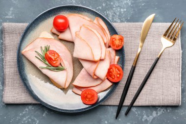 Plate with slices of tasty ham, tomatoes and rosemary on grey grunge background