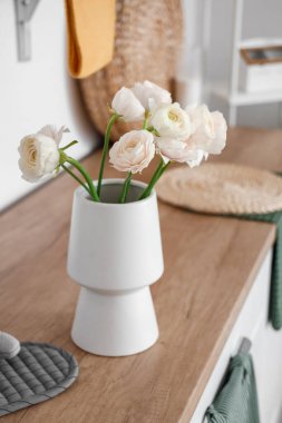 Mutfaktaki tezgahın üzerinde ranunculus çiçekleri olan vazo.