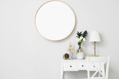 Vazo, ranunculus çiçekleri, lamba, çalar saat ve ışık duvarının yanındaki masada dekor.