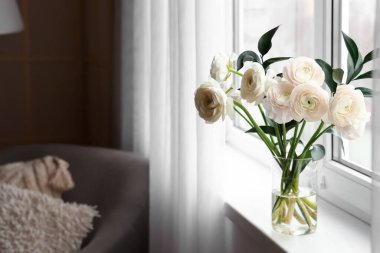 Vase with ranunculus flowers on windowsill in room, closeup