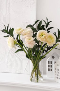 Vazo, ranunculus çiçekleri, mum tutacakları ve şöminenin üzerinde resim.