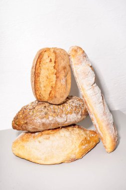Loaves of different bread on table white wall