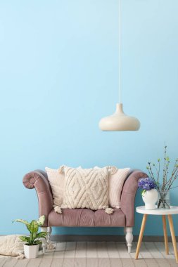 Mavi duvarın yanında yastıklı, masalı ve farklı bitkilerden oluşan rahat bir kanepe.