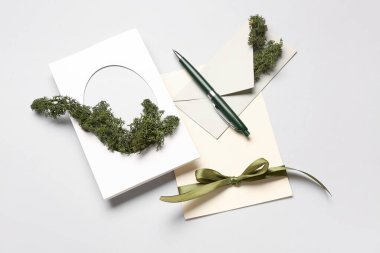 Beyaz arkaplanda kart, zarf, kalem ve yosun içeren kompozisyon