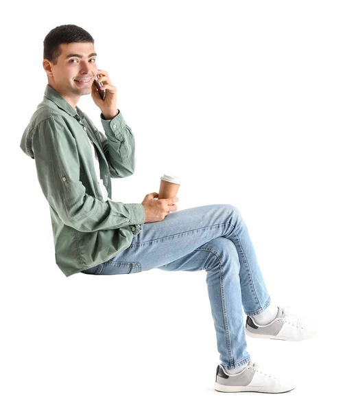 坐在白色背景的椅子上 一边喝咖啡一边用手机聊天的年轻人 — 图库照片