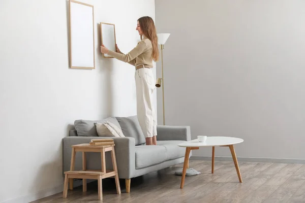 Young Woman Hanging Blank Frame Light Wall Home — Zdjęcie stockowe