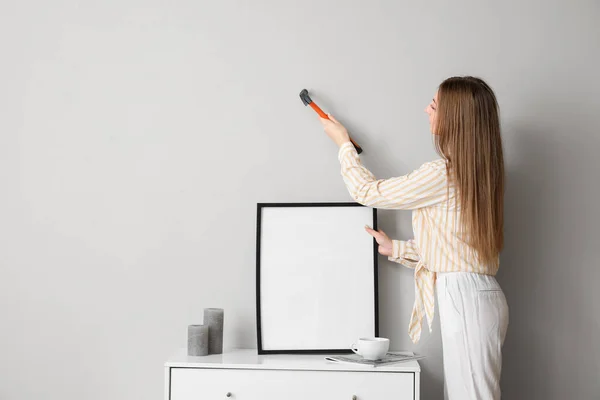 Young Woman Hanging Blank Frame Grey Wall Home — Zdjęcie stockowe