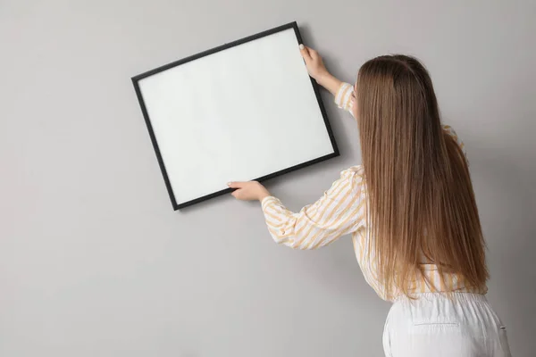 Young Woman Hanging Blank Frame Grey Wall Home — Stock Photo, Image