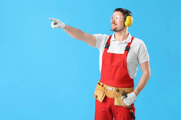 Homem Carpinteiro Protetores Auditivos Apontando Para Algo Fundo Azul — Fotografia de Stock