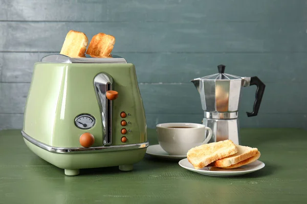 stock image Modern toaster with crispy bread slices, geyser coffee maker and cup of espresso on green wooden table