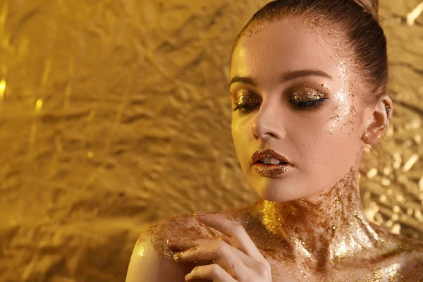 Young woman with golden glitter makeup on yellow foil background, closeup