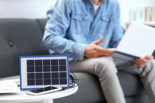 stock image Portable solar panel charging mobile phone on table in room, closeup