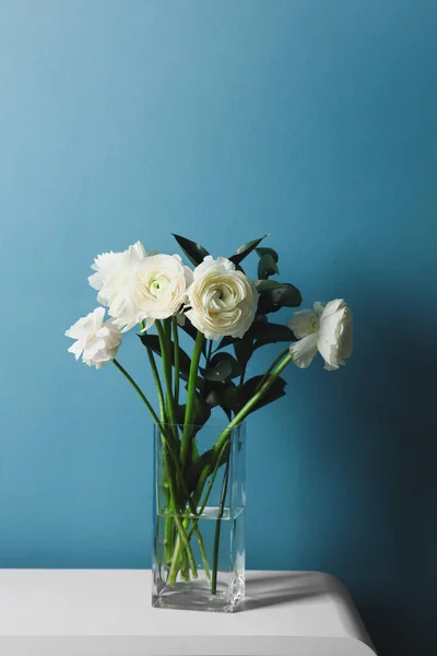 Vase with ranunculus flowers on table near blue wall