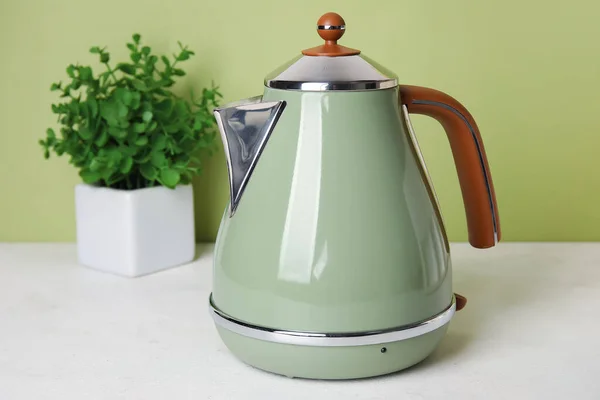 Electric kettle on table near green wall, closeup