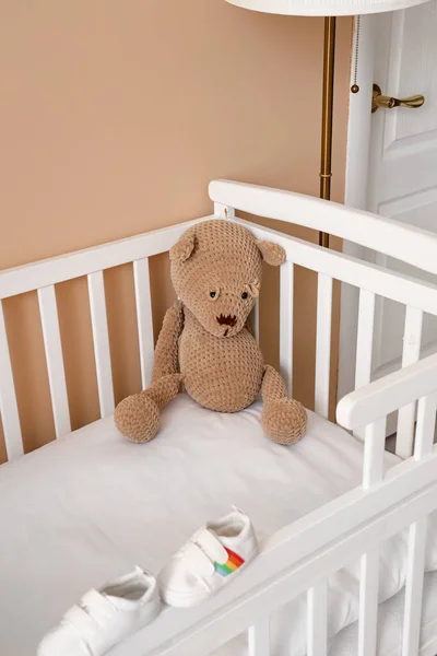 Crib with toy bear and baby booties in bedroom, closeup
