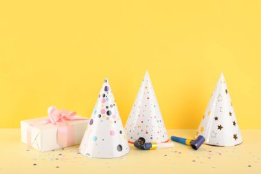 Sarı duvarın yanındaki masanın üzerinde hediye kutusu olan parti dekoru.