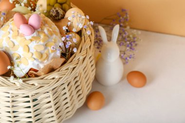 Paskalya yumurtalı sepet, pasta, çingene çiçekleri ve tavşancık bej arka planda beyaz masanın üzerinde.
