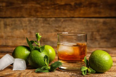 Bir bardak buzlu rom, ahşap masada nane ve limon.