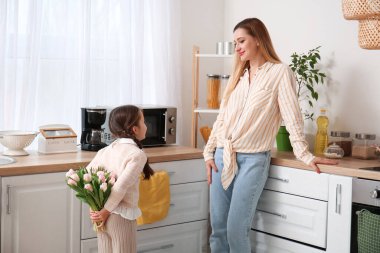 Sevimli küçük kız annesini mutfakta lalelerle selamlıyor.