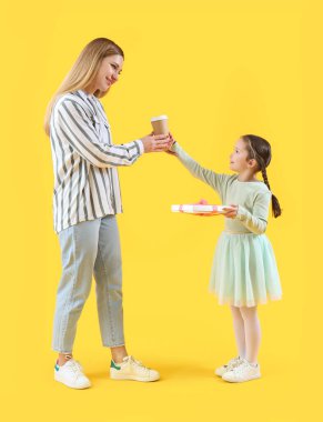 Sevimli küçük kız, sarı arka planda annesine hediye ve bir fincan kahveyle selam veriyor.