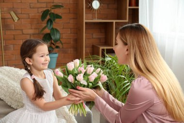 Sevimli küçük kız, annesini lalelerle selamlıyor.