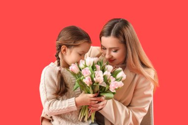 Sevimli küçük kız annesini kırmızı arka planda lalelerle selamlıyor.