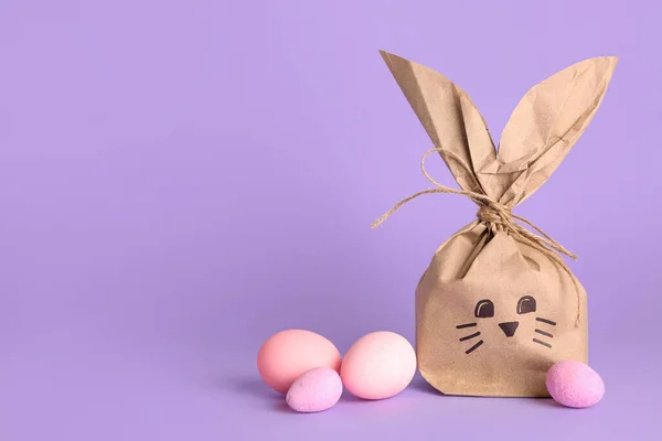 紫丁香背景的兔子礼品袋和复活节彩蛋 — 图库照片