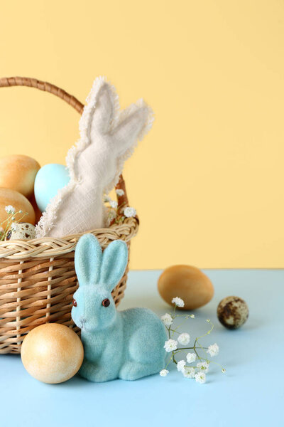 Basket with Easter eggs, bunnies and gypsophila flowers on blue table against beige background