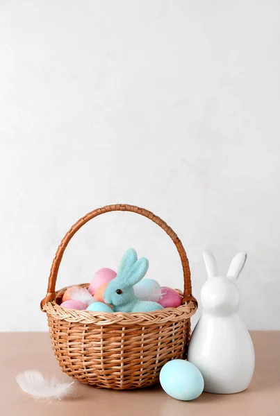 stock image Basket with Easter eggs and bunnies on beige table against white background