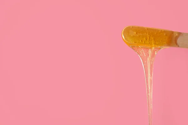 Spatula with sugaring paste on pink background, closeup