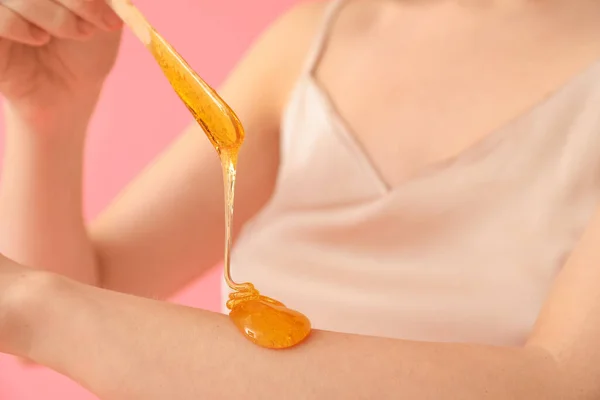 Young woman applying sugaring paste onto her arm against pink background, closeup