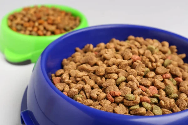 Bowls of dry pet food on white background, closeup