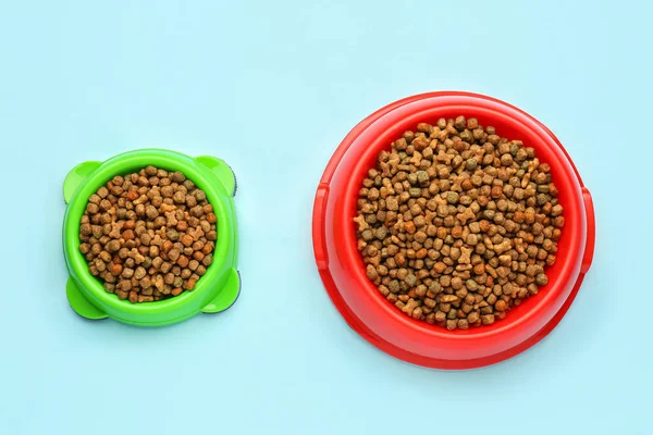 stock image Bowls of dry pet food on color background