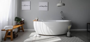 Modern bathtub with wooden bench near grey wall clipart