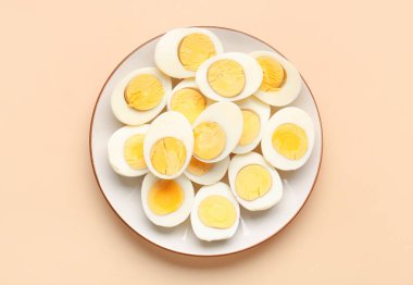 Plate with halves of delicious boiled eggs on beige background