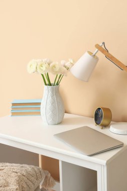 Vazoda ranunculus çiçekleri ve bej duvarın yanında lamba olan işyeri