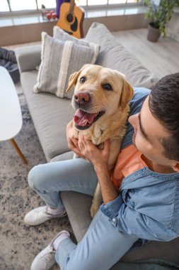 Labrador köpeği olan genç adam evdeki kanepede oturuyor.