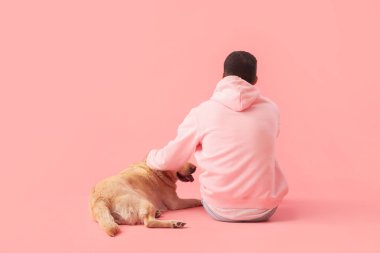 Labrador köpeği olan genç bir adam pembe arka planda oturuyor.