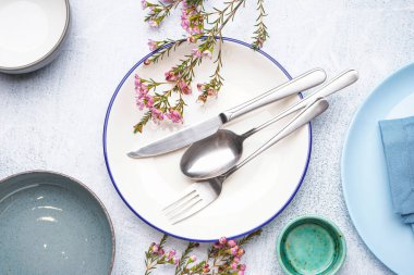 Temiz tabaklar, çatal bıçak takımı ve gri grunge arka planda çiçek dekoru olan kompozisyon