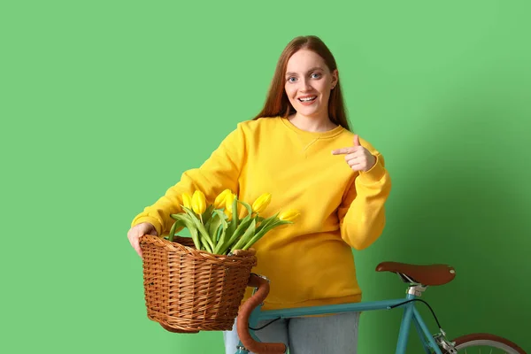 年轻女子 骑自行车指着绿色背景的篮子里的郁金香 — 图库照片