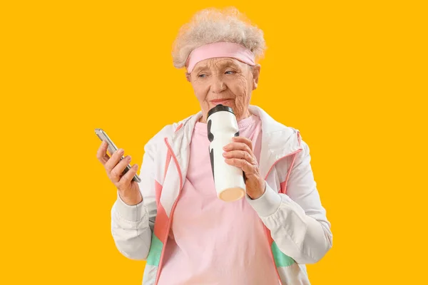 Sportowa Seniorka Telefonem Komórkowym Butelką Wody Żółtym Tle — Zdjęcie stockowe