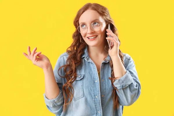 美しい赤毛女性の話によって携帯電話上の黄色の背景 — ストック写真