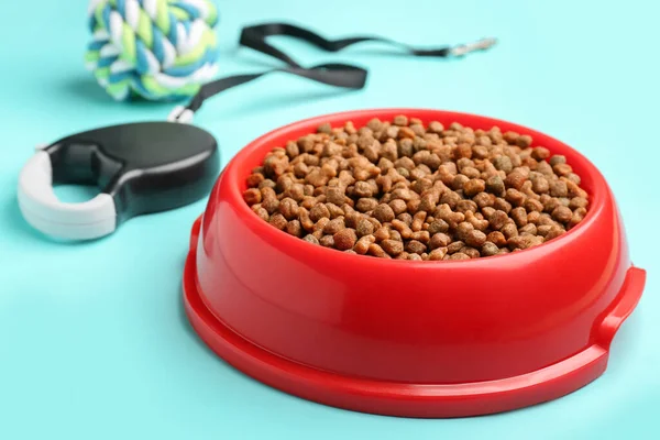 Bowl of dry pet food and leash on color background, closeup